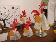 three roosters made out of folded paper on a table next to a candle holder