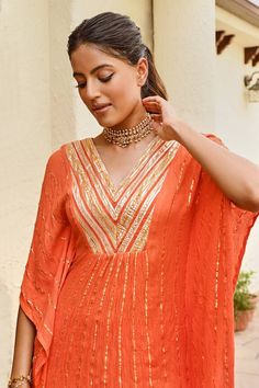 Orange flared sleeve kaftan with golden stripe pattern. Paired ivory lurex sharara.
Components: 2
Pattern: Stripe
Neckline: V Neck
Sleeve Type: Flared Sleeves
Fabric: Rayon Crepe Lurex
Color: Orange
Other Details: 
Kaftan:
Zari work yoke
Occasion: Sangeet - Aza Fashions Festive Party Kaftan With Gota Work, Traditional Drape Kaftan With Gota Work For Parties, Anarkali Style Gota Work Kaftan For Festive Occasions, Party Kaftan With Gota Work And Traditional Drape, Bollywood Style Kaftan With Gota Work For Party, Navratri Party Kaftan With Gota Work, Elegant Kaftan With Gota Work For Festivals, Elegant Kaftan With Gota Work For Eid, Elegant Gota Work Kaftan For Eid