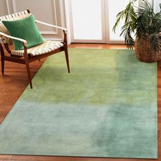 a living room area with a chair and rug on the wooden floor, next to a potted plant