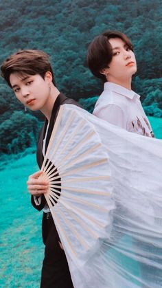 two young men standing next to each other while holding an umbrella in front of them