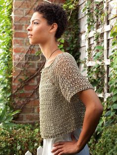 a woman standing in front of a brick wall with her hands on her hips and looking off to the side