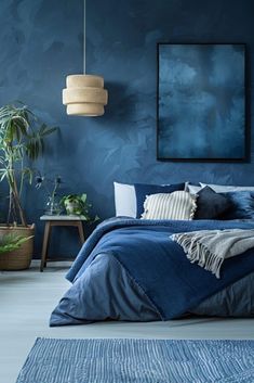 a bed with blue sheets and pillows in front of a painting on the wall above it