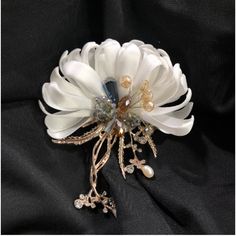 a brooch with white flowers and pearls on it's center piece, sitting on a black cloth