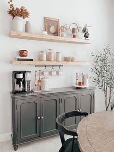 a dining room table and some shelves with cups on it, coffee maker and other items