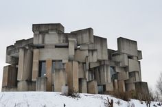 a building made out of concrete blocks on top of a snow covered hill with trees in the background