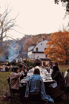 a group of people sitting around a long table in the middle of a yard eating