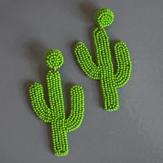 two green beaded cactus earrings sitting on top of a gray table next to each other