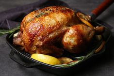 a roasted chicken in a pan with lemons and rosemary