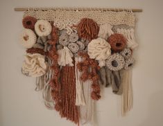 a wall hanging with crocheted flowers and yarns on the bottom, along with wooden pegs