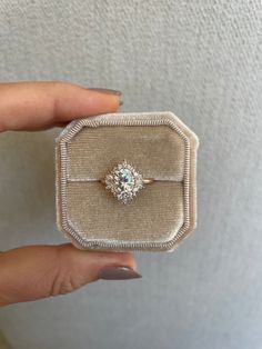 a woman's hand holding an engagement ring in a velvet box with a diamond center