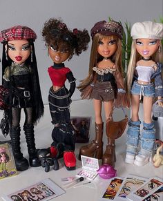 four dolls are standing next to each other on a table with cards and pictures around them