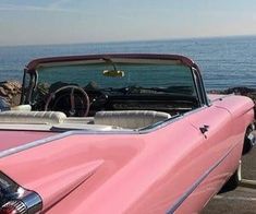 an old pink convertible car parked next to the ocean with its hood up and open