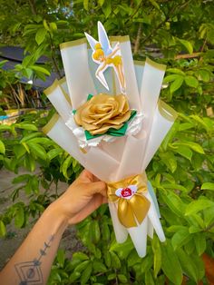 a person holding up some paper flowers in their hand with gold and white ribbons on them