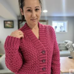 a woman wearing a pink crocheted cardigan standing in front of a table