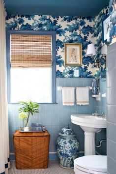 a bathroom with blue and white wallpaper has a bamboo basket on the counter next to the toilet