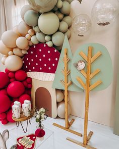 a table topped with lots of balloons next to a wall filled with trees and houses