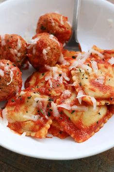 a white plate topped with ravioli and meatballs next to a fork on top of a wooden table