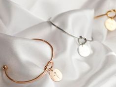 two gold and silver bracelets with personalized tags on them sitting on a white cloth