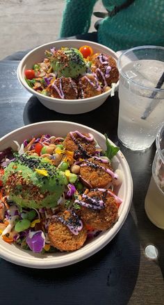 two white bowls filled with food on top of a table next to a glass of water