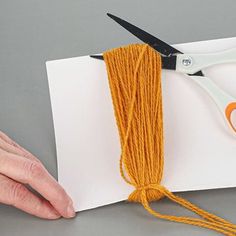 a pair of scissors and yarn on top of a piece of white paper with orange thread