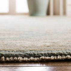 an area rug on the floor with a vase in the background