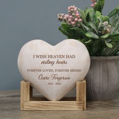 a heart shaped memorial stone on a wooden stand next to a potted plant