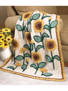 a crocheted blanket with sunflowers on it next to a white vase