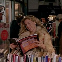 a woman is reading a book in front of a bookshelf full of books