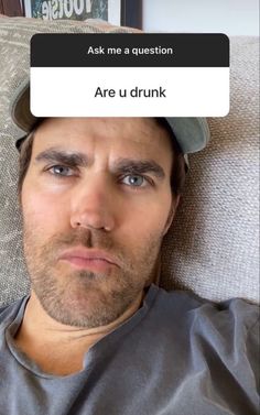 a man laying on top of a couch wearing a baseball cap and looking at the camera