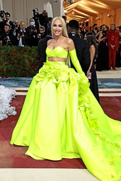 a woman in a bright yellow dress standing on a red carpet with cameras around her