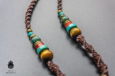 "Handmade ethnic necklace for Men and Women. A unique piece in a boho, Indian style. Made with the macramé technique using dark brown cotton threads. Midway decorated with beautiful natural stones (Coral, Lapis Lazuli, and Turquoise stones). The beautiful central pendant from India is of a dark brown shade, decorated with bronze linings and pieces of turquoise and red ceramic. In the middle an ancient Sanskrit symbol. The closure is a sliding macramé knot that permits you to adjust the necklace Tibetan Necklace, Macrame Colar, Om Pendant, Red Ceramic, Brown Shade, Ethnic Necklaces, Boho Macrame, Unisex Necklace, Boho Pendant