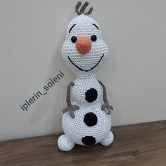 a crocheted snowman sitting on top of a wooden table next to a wall