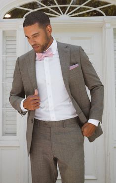 a man in a gray suit and pink bow tie is looking down at his pocket