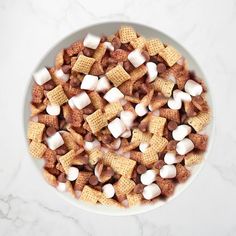 a white bowl filled with marshmallows and chex mix on top of a marble counter