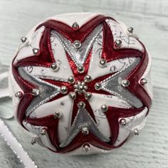 a white and red ornament with silver beads on it's side sitting on a table