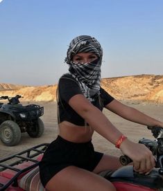 a woman riding on the back of a red four - wheeler with a bandanna over her head