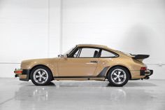 an old yellow porsche sits in a white room next to a brick wall and floor