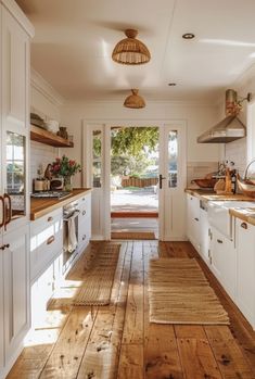 an open kitchen with wooden floors and white cupboards on the walls, along with lots of natural wood flooring