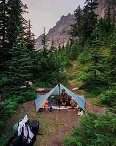 a tent pitched up in the woods with trees around it and camping gear on the ground