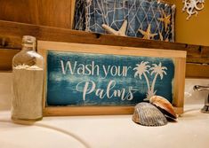 a wooden sign that says wash your palms next to a seashell on a bathroom sink