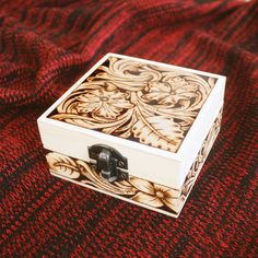 a small wooden box sitting on top of a red cloth covered tablecloth with an intricate design