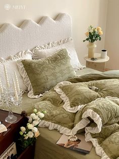 a bed with green comforter and pillows on top of it next to a nightstand