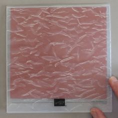 a hand holding a clear plastic bag with pink paper on it's bottom and side