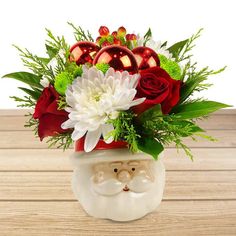 a vase filled with red roses and white flowers next to a santa clause head on a wooden table