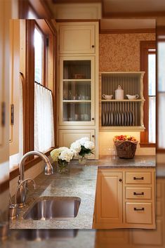 a kitchen with marble counter tops and white cabinets, along with flowers in the window sill