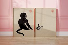 two canvases with black cats on them in front of a pink wall and floor