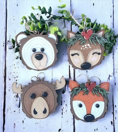 four wooden animal ornaments are hanging on a white wood plank wall with greenery around them