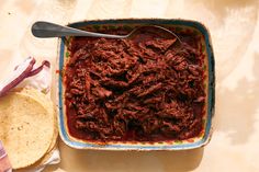 a bowl of shredded meat and tortillas on a table