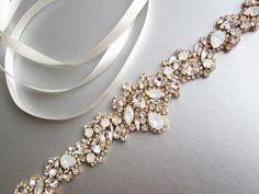 "This exquisite vintage inspired belt features Swarovski crystal design in opal and clear crystal mix. The crystal design measures 14 1/2\" long and 1 3/4\" wide in the center. The satin ribbon measures 3/8\" wide and 150\" long. Available is gold or silver finish and with a variety of ribbon options. Shown in the photos with light ivory satin ribbon and in gold finish. - For the photo of the grossgrain ribbon color options, please take a look here: https://www.etsy.com/listing/231071205/grosgra Elegant White Belt With Rhinestones, White Crystal Sash For Formal Occasions, White Crystal Sashes For Formal Occasions, Formal White Crystal Sash, White Rhinestone Bridal Belt For Evening, Evening White Bridal Belt With Rhinestones, Gold Rhinestone Belt For Formal Occasions, White Bling Bridal Belt For Wedding, Elegant Bling Bridal Belt For Wedding