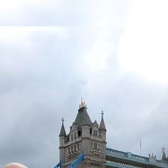 a person holding up a cell phone in front of a tower bridge with flags on it